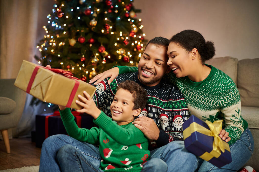 vreugdevolle liefdevolle Afrikaanse Amerikaanse familie uitwisselen van cadeautjes en knuffelen warm op kerstavond - Foto, afbeelding