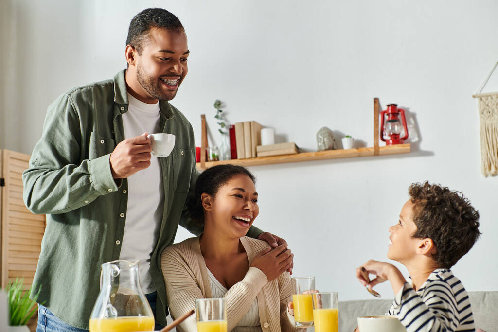カジュアルな家庭での陽気なアフリカ系アメリカ人の家族は,おいしい朝食を食べて,肩に手をつけます - 写真・画像