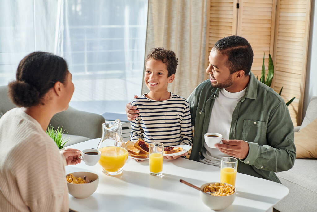 gelukkig vreugdevol Afrikaans amerikaanse ouders kijken liefdevol naar hun kleine zoon aan tafel ontbijt - Foto, afbeelding