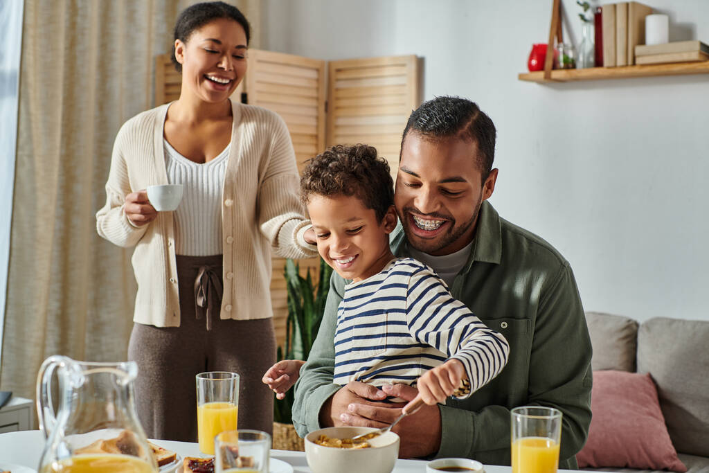joyful modern african american family eating breakfast and drinking coffee and orange juice together - Photo, Image
