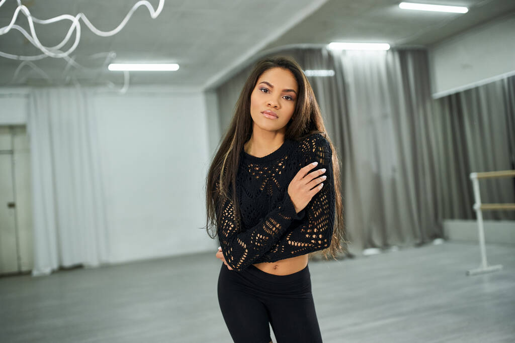 charming long-haired african american woman in black crop sweater dancing and looking at camera - Photo, Image