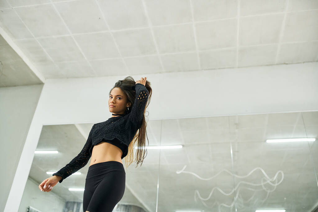 приваблива довгошерста афроамериканка в чорному одязі репетиції в танцювальній студії - Фото, зображення