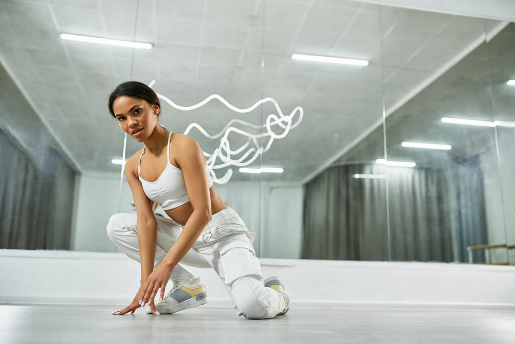 dançarina americana africana na moda em top de esportes brancos e calças olhando para a câmera no estúdio de dança - Foto, Imagem