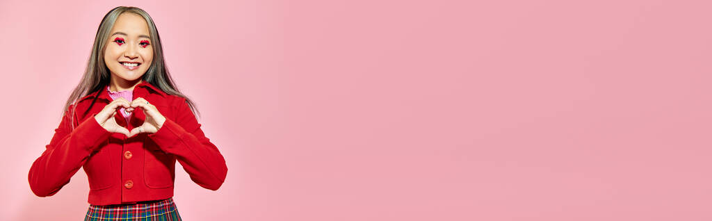 San Valentino banner, felice ragazza asiatica con gli occhi rossi trucco mostrando il cuore con le mani sul rosa - Foto, immagini
