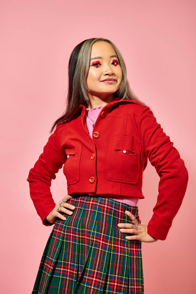 Valentinstag Konzept, glückliche asiatische Mädchen in roter Jacke posiert mit den Händen auf Hüften auf rosa Hintergrund - Foto, Bild
