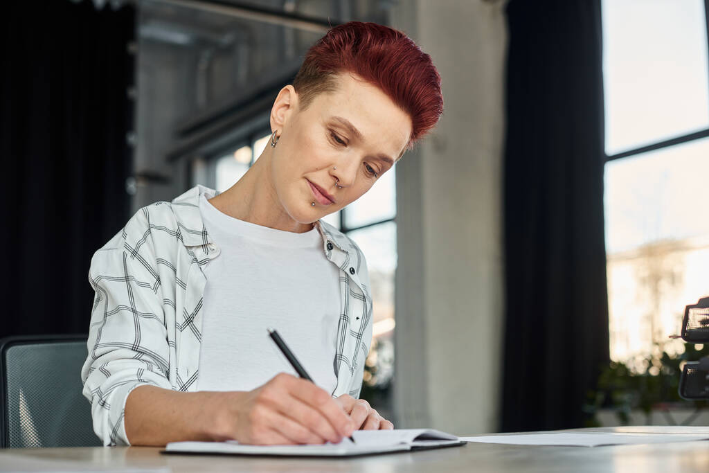 soustředěný stylový bigender osoba sedí na pracovišti v moderní kanceláři a psaní v notebooku - Fotografie, Obrázek