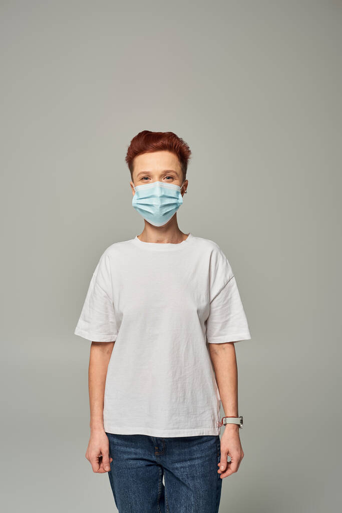 positive rousse queer personne gagner blanc t-shirt et masque médical debout sur fond gris - Photo, image