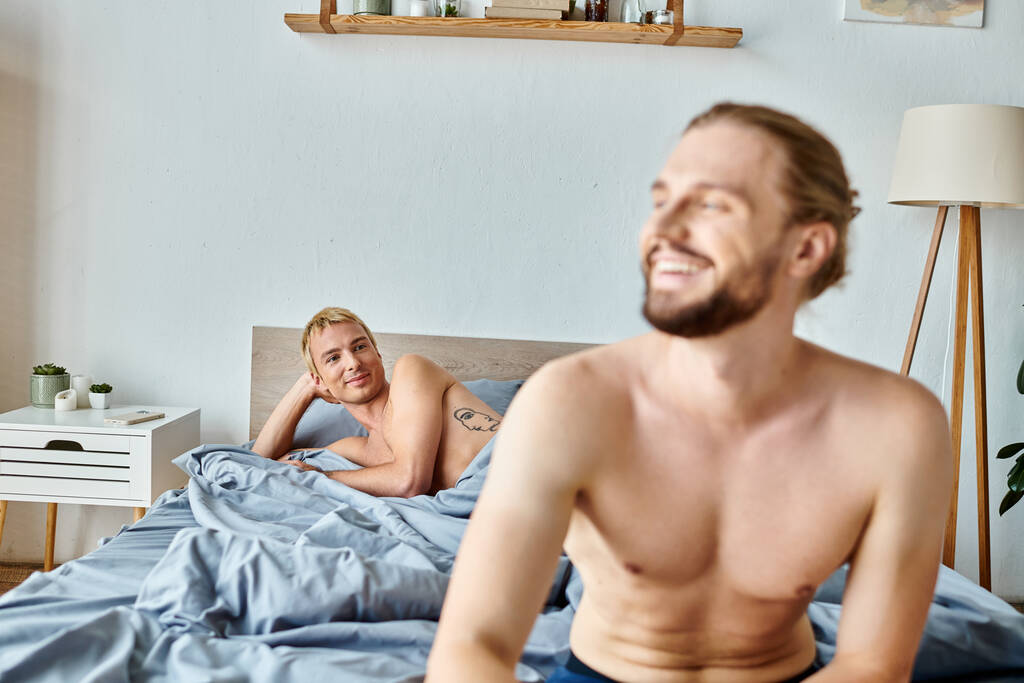 cheerful bearded gay man looking away near love partner lying in bedroom, harmonious relationship - Photo, Image
