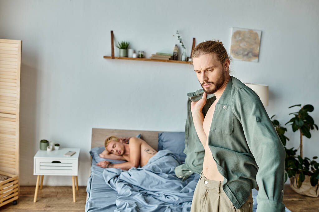 Hüsrana uğramış sakallı eşcinsel adam erkek arkadaşının yanında giyiniyor. Sabahları yatak odasında uyuyor. Aşk çatışması. - Fotoğraf, Görsel