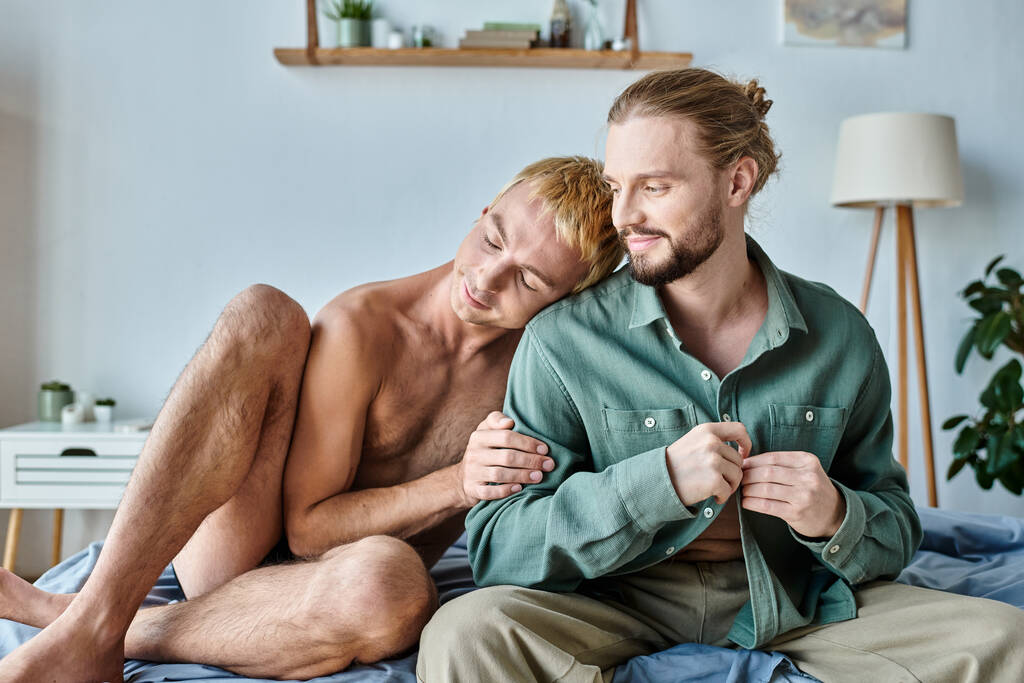 щасливий гей чоловік спирається на усміхненого бородатого хлопця, що сидить у сучасній спальні, щастя - Фото, зображення