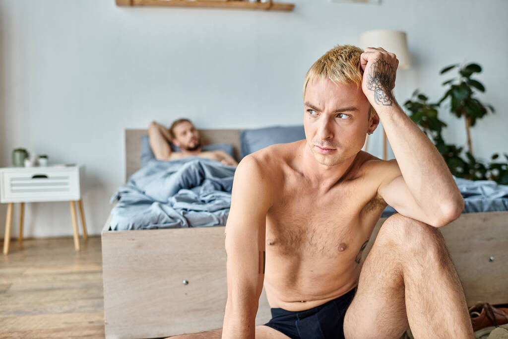 offended tattooed gay man looking away near love partner lying in bedroom in morning, troubled love - Photo, Image