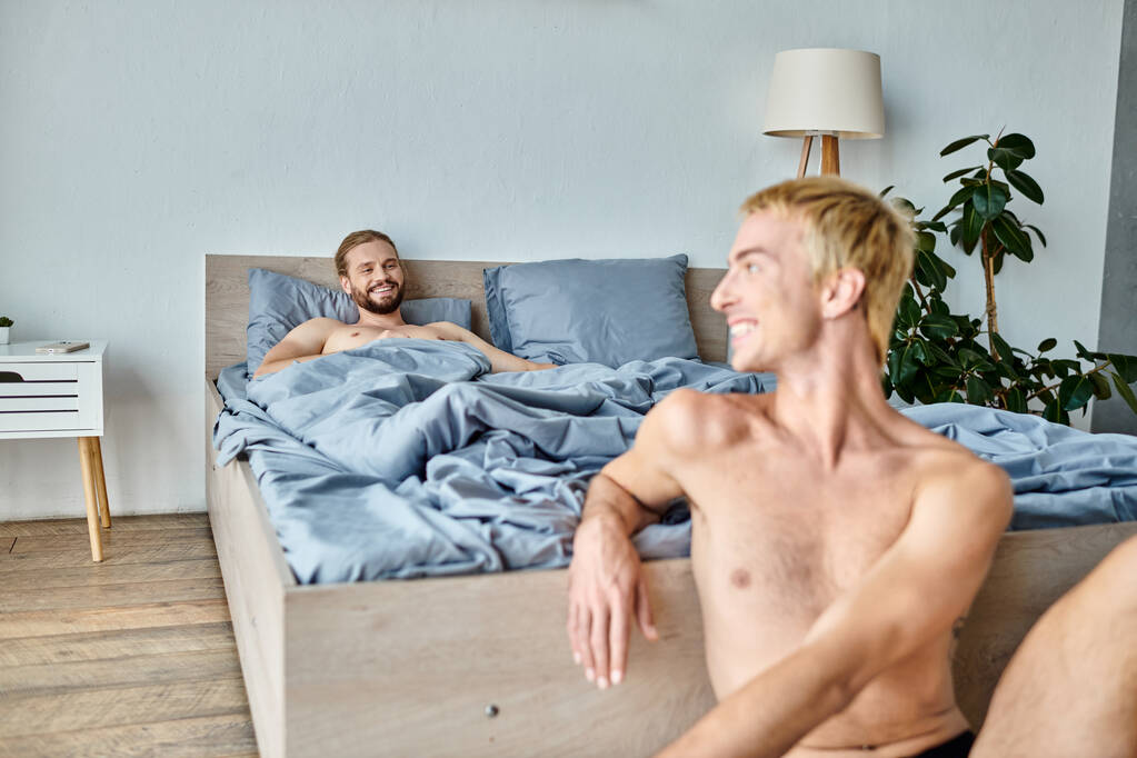 iloinen parrakas homo mies makaa sängyllä ja katselee hymyilevä poikaystävä aamulla, onnellinen makuuhuone kohtaus - Valokuva, kuva