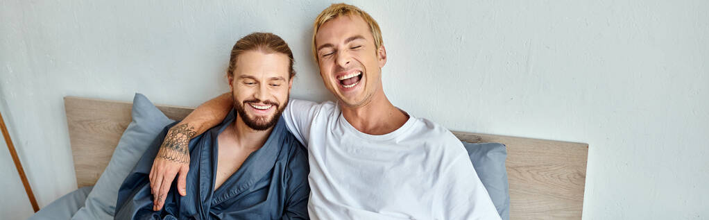 vrolijk gay paar lachen terwijl zitten op bed in de ochtend, gelukkig relaties, horizontaal banner - Foto, afbeelding