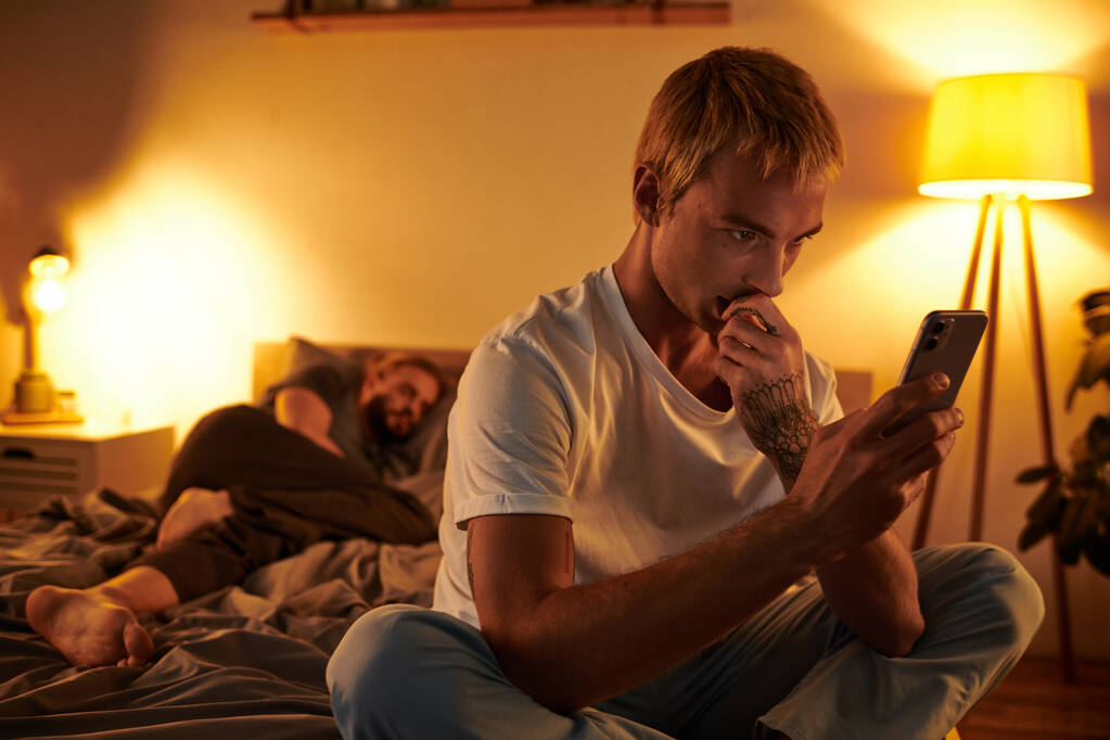 untreuer schwuler Mann chattet auf Handy in der Nähe von Liebespartner, der nachts im Schlafzimmer schläft - Foto, Bild