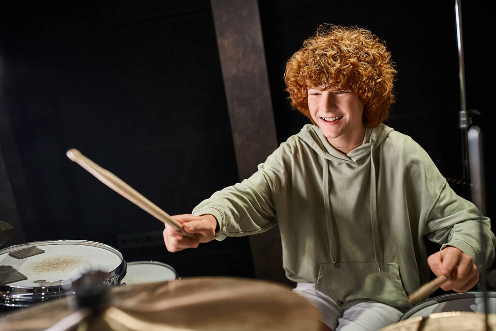 vrolijk schattig talentvolle tiener jongen in casual outfit spelen zijn drums actief in de studio - Foto, afbeelding