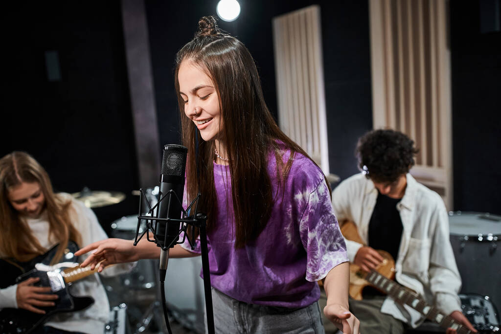 alegre morena adolescente cantando felizmente con sus amigos tocando instrumentos en estudio - Foto, Imagen