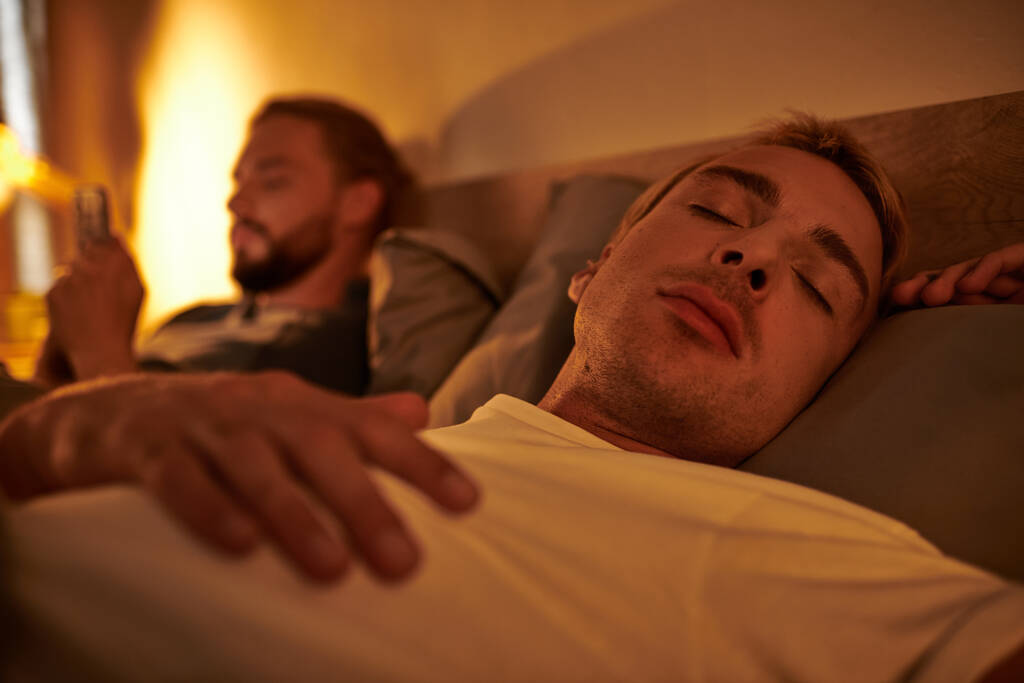 gay hombre durmiendo cerca infiel novio navegación fecha aplicación en smartphone en la noche en dormitorio - Foto, imagen