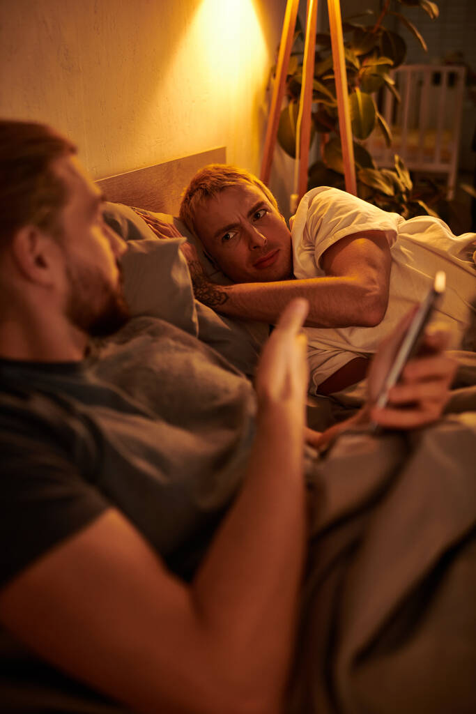 desleal gay hombre navegación fecha aplicación en smartphone cerca desalentado novio en la noche en dormitorio - Foto, Imagen