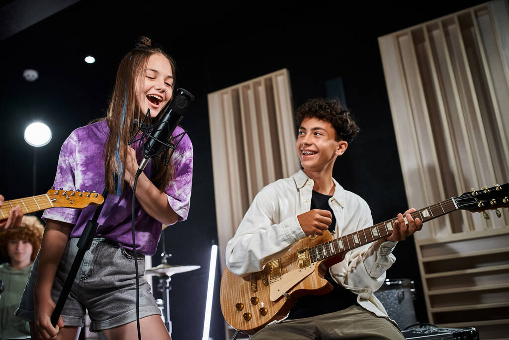 alegres adolescentes talentosos en trajes casuales cantando y tocando guitarras mientras están en su estudio - Foto, Imagen