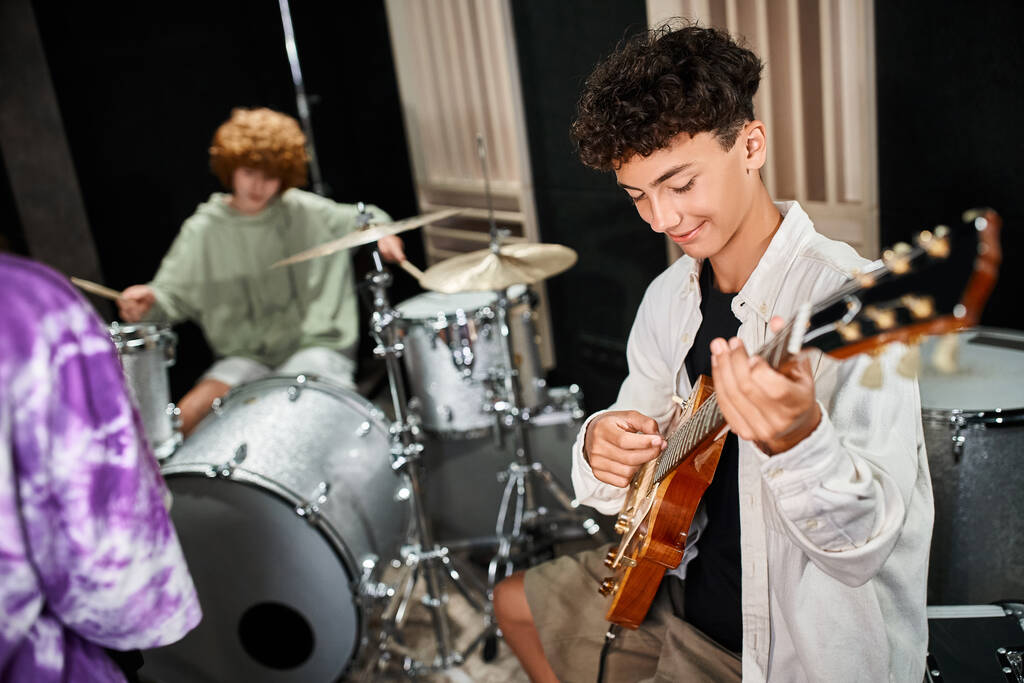 Fokus auf fröhliche niedliche Teenager, die aktiv neben ihren verschwommenen Bandmitgliedern Gitarre spielen - Foto, Bild