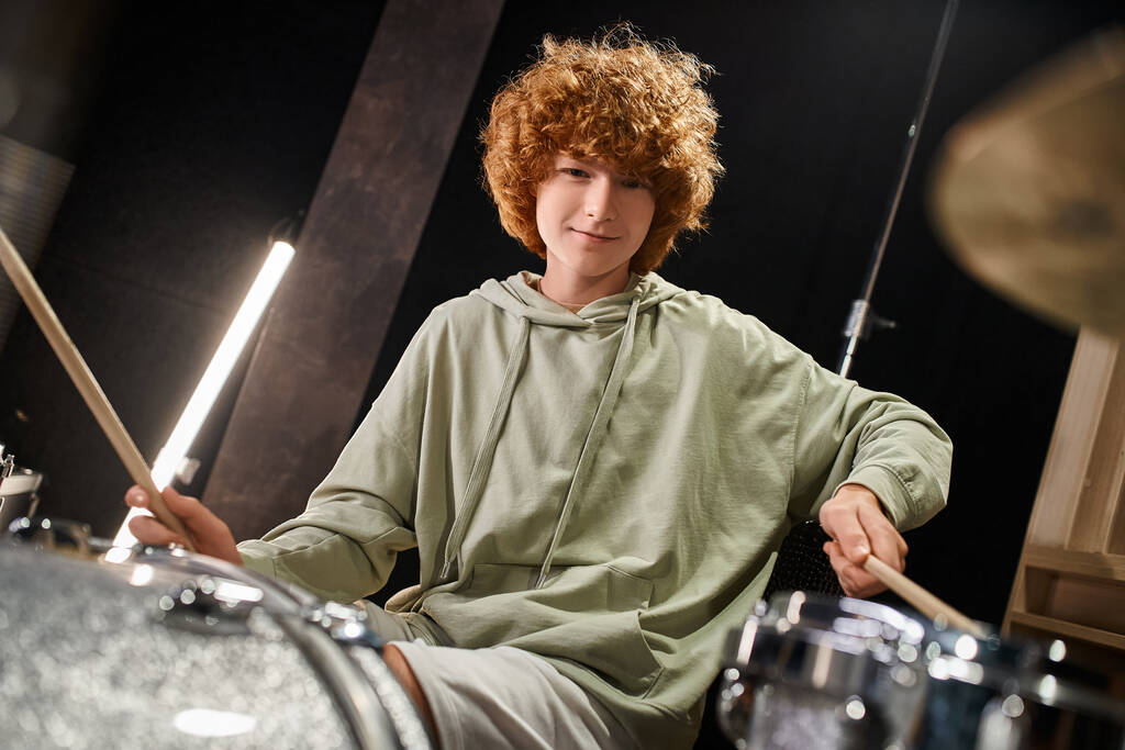 happy cute red haired teenage boy in everyday outfit playing his drums and looking at camera - Photo, Image