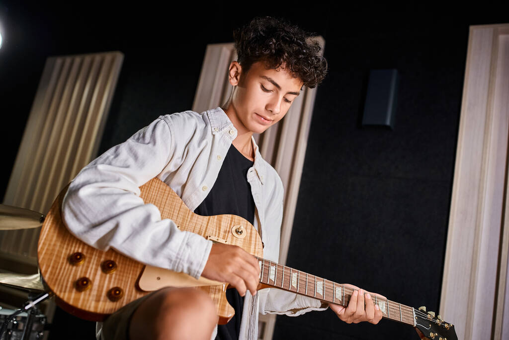 konzentrierter talentierter, entzückender Teenager im lässigen Outfit, der im Studio seine Gitarre spielt - Foto, Bild