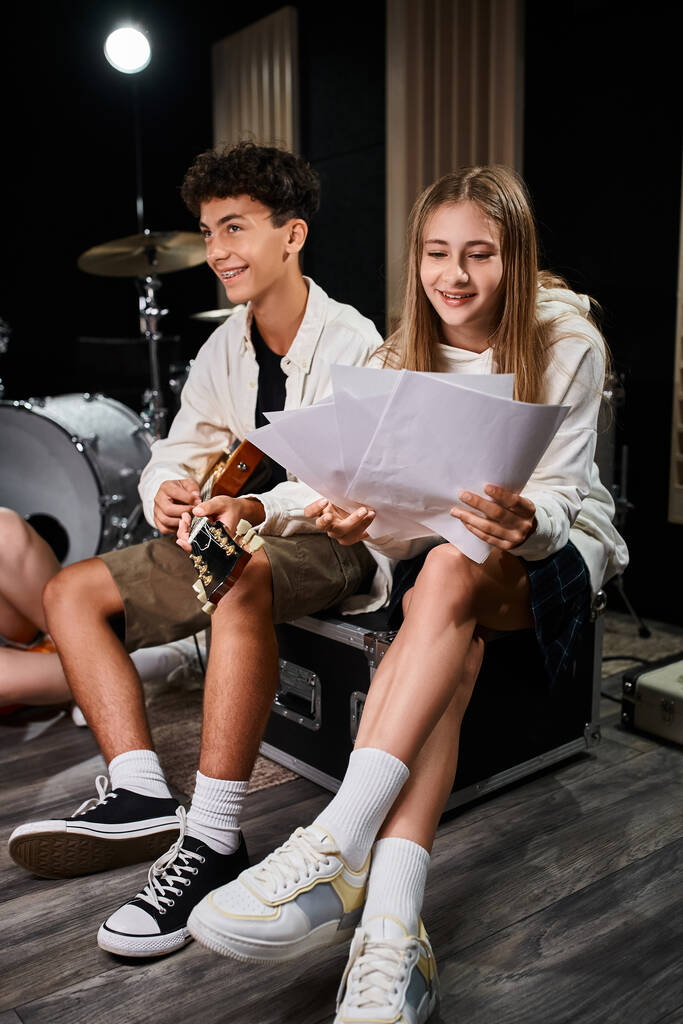 alegre adolescente mirando letras al lado de su amigo con frenos tocando la guitarra, grupo musical - Foto, Imagen