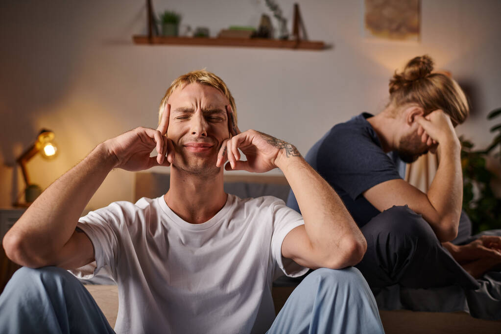 deprimido gay homem sentado com fechado olhos perto namorado no quarto no noite, perturbado relacionamento - Foto, Imagem