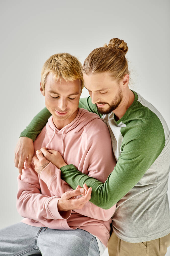 romantický a smyslný homosexuální pár ve stylovém neformálním oblečení objímající se na šedém pozadí, gay láska - Fotografie, Obrázek