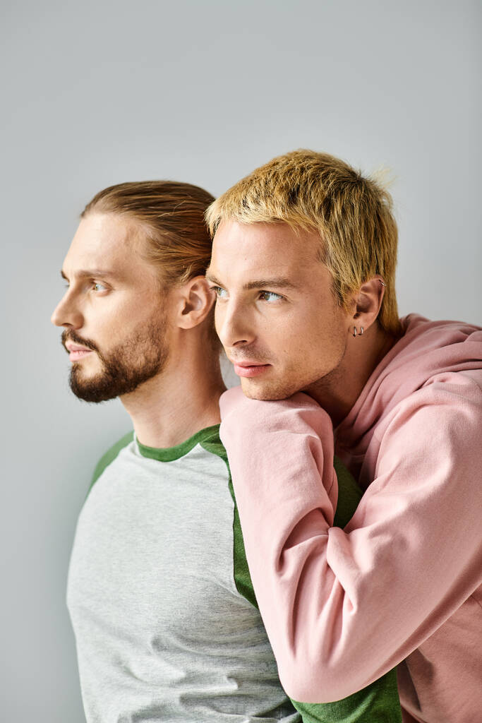 romántico pareja gay de ensueño en traje casual de moda mirando hacia otro lado en gris telón de fondo, armonía y amor - Foto, imagen