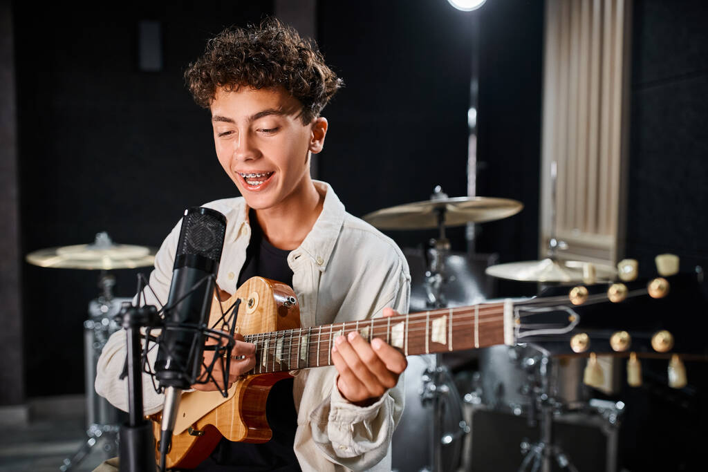 talentierter süßer Teenager in lässiger Kleidung, der im Studio Gitarre spielt und Lieder ins Mikrofon singt - Foto, Bild
