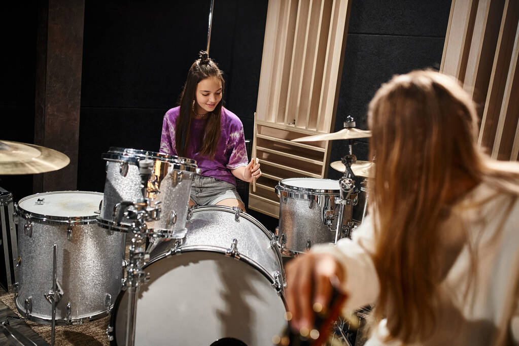 весела чарівна дівчина-підліток грає на барабанах, а її подруга блондинка дивиться на неї, музична група - Фото, зображення