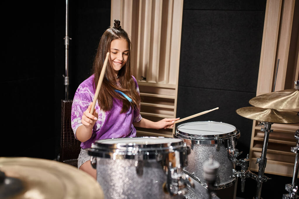 csinos barna tini lány élénk alkalmi öltözékben dobolás közben a zenei stúdióban - Fotó, kép