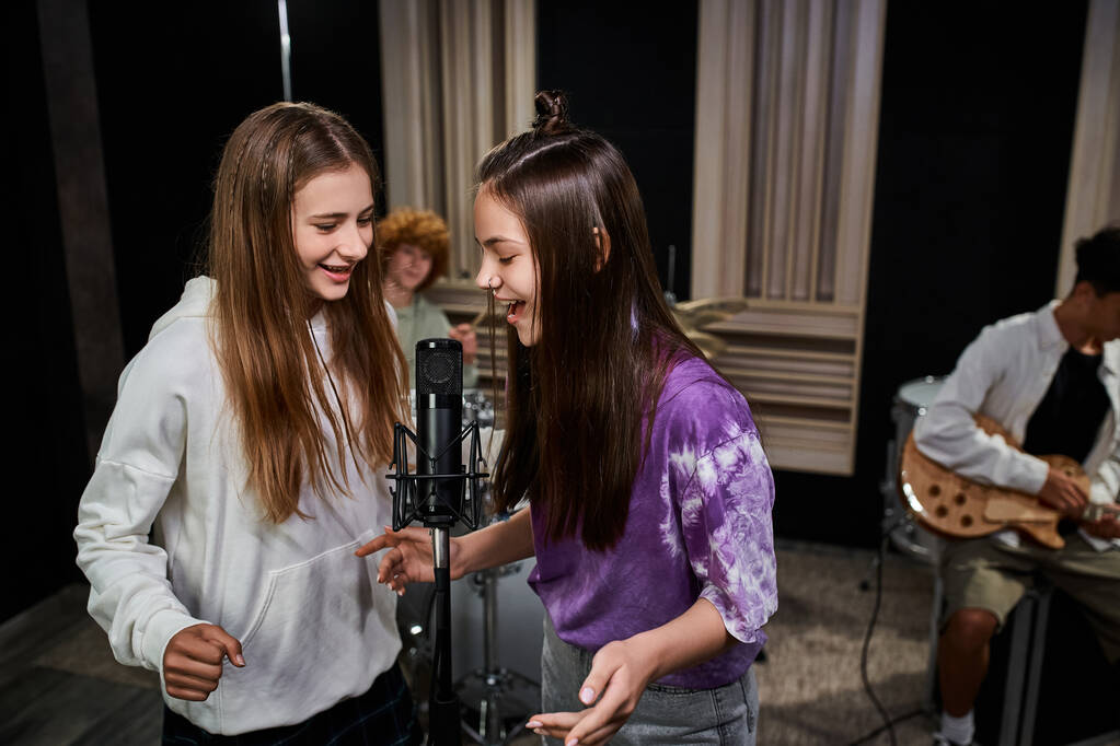 csinos tizenéves lányok énekelnek mikrofonba, míg a fiúk dobolnak és gitároznak, zenei csoport - Fotó, kép