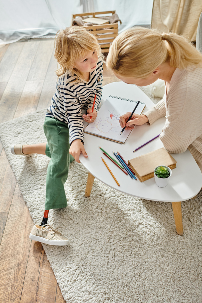 madre y niño con la pierna protésica dibujando juntos en papel con lápices de colores, tiempo de calidad - Foto, Imagen