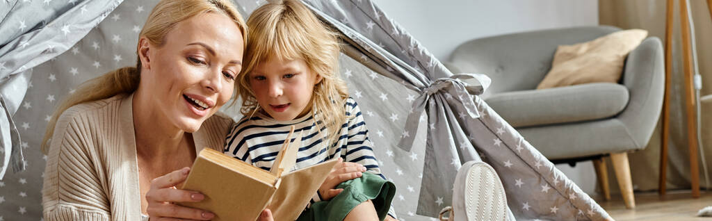 cute preteen girl and blonde mother reading book and sitting together in play tent at home, banner - Photo, Image