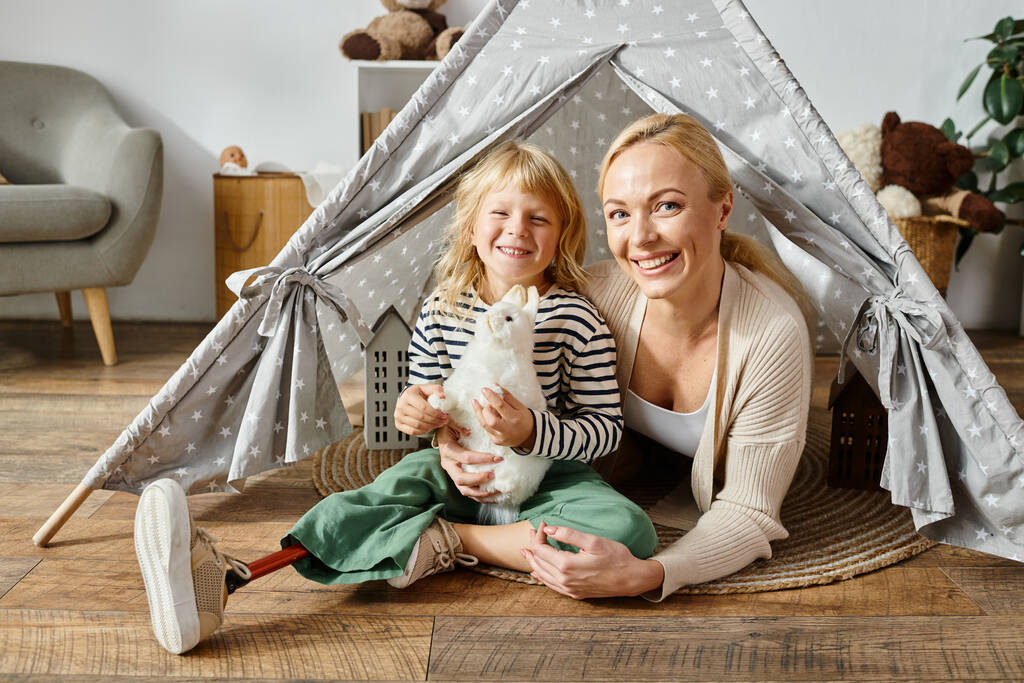遊びのテントの母親の近くに柔らかいおもちゃを保持する義足の幸せな少女の家族の肖像画 - 写真・画像