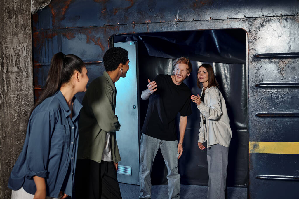 cheerful young man gesturing and inviting friends to subway wagon inside of escape room, quest - Photo, Image