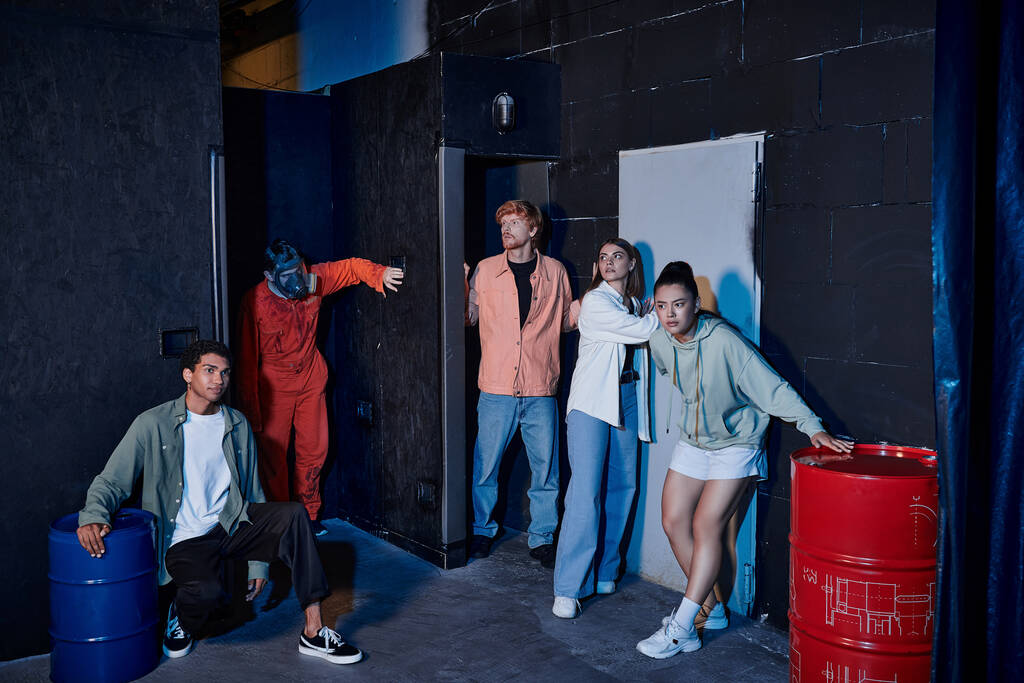 grupo interracial de amigos escapando de homem com máscara de gás durante a aventura na sala de busca - Foto, Imagem