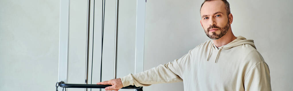 vousatý mužský pacient stojící u cvičícího stroje v tělocvičně moderního kineziologického centra, prapor - Fotografie, Obrázek