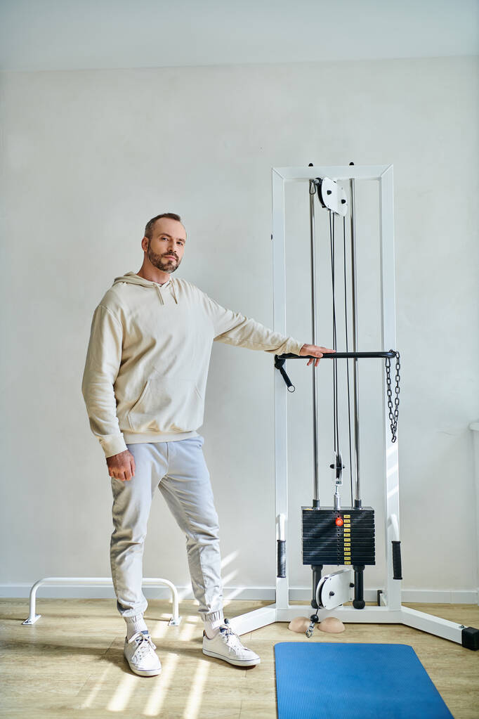 longitud completa del hombre guapo cerca de la máquina de ejercicio en el gimnasio del centro moderno de kinesiología - Foto, imagen