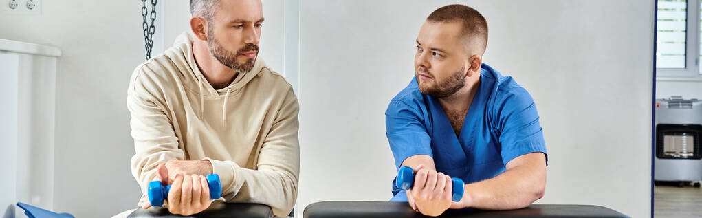 médecin en uniforme bleu et son patient masculin faisant de l'exercice avec haltères au centre kinesio, bannière - Photo, image