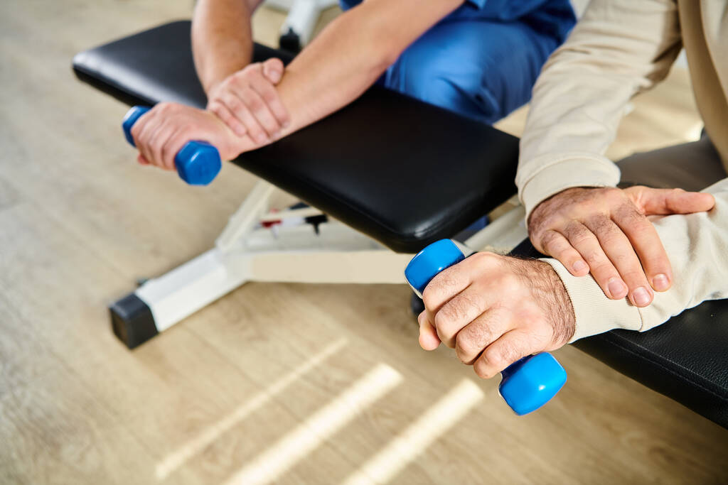 vista recortada del paciente masculino haciendo ejercicio con mancuerna cerca de especialista de recuperación en el centro de kinesio - Foto, Imagen