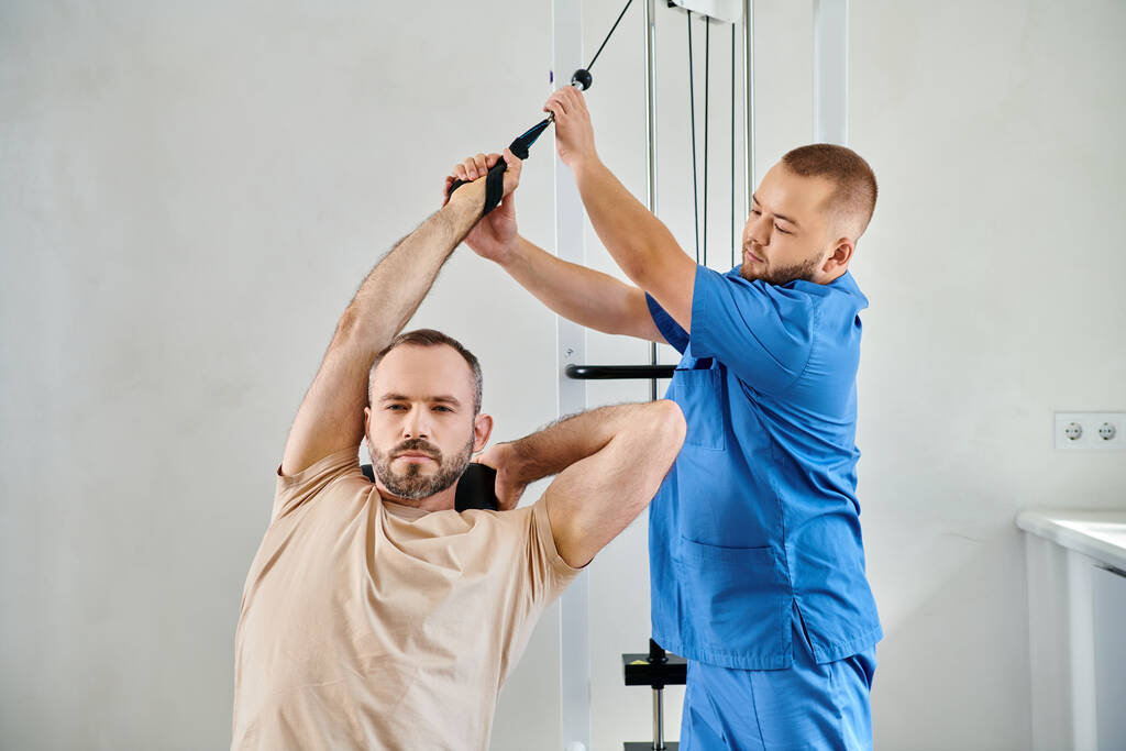 instrutor profissional apoiando o homem trabalhando na máquina de exercício no ginásio do centro de kinesio - Foto, Imagem