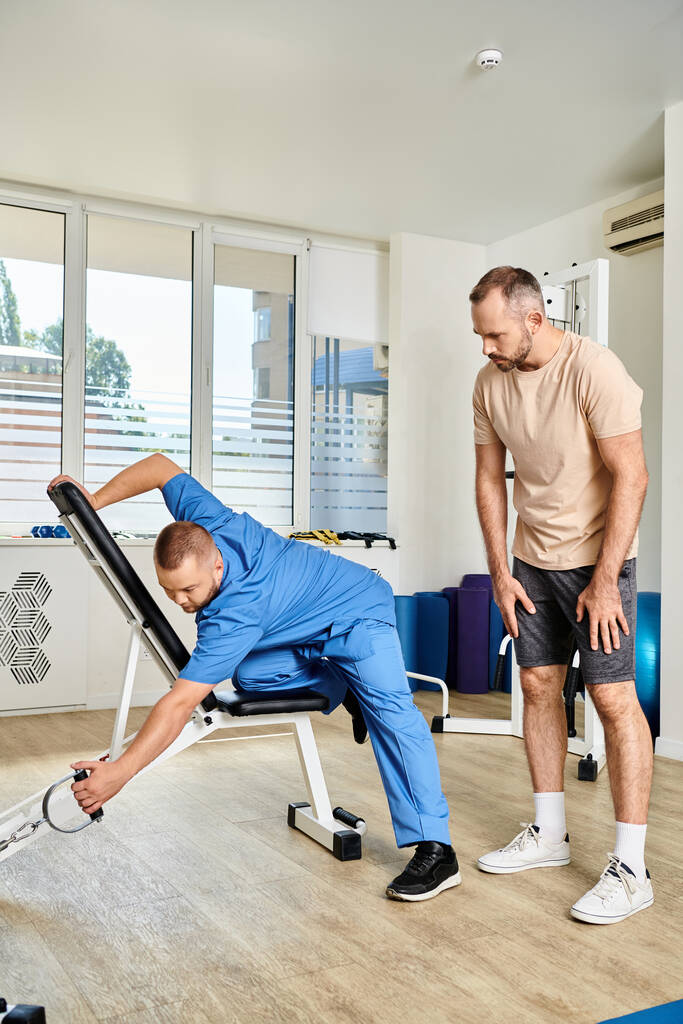специалист по восстановлению в синей форме, показывающий, как тренироваться на тренажере в центре кинезиологии - Фото, изображение