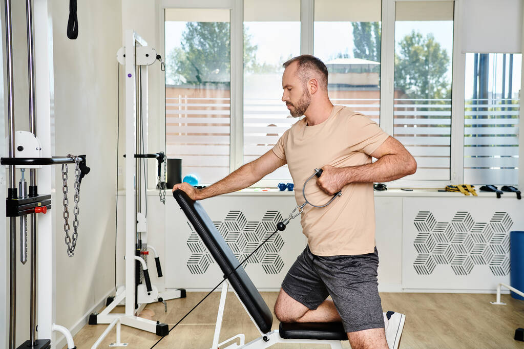 Seitenansicht des bärtigen Mannes in Sportbekleidung beim Training an einem Trainingsgerät, Erholung im Kinesio-Zentrum - Foto, Bild