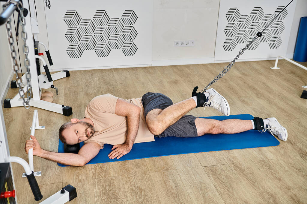 wysoki kąt widzenia człowieka leżącego na macie fitness i treningu na urządzeniu treningowym w centrum kinesio - Zdjęcie, obraz