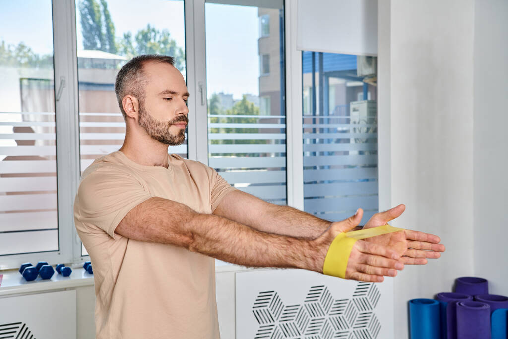 pohledný vousatý muž trénink s páskou odporu v kineziologickém centru, zotavení - Fotografie, Obrázek