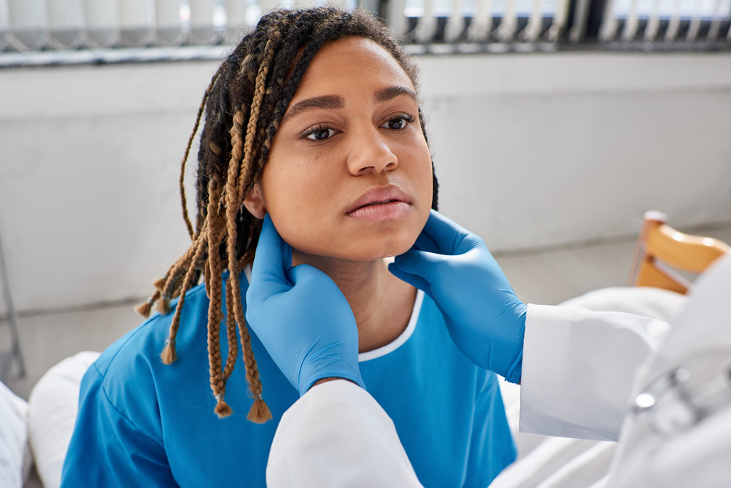 mladá africká americká žena při pohledu na svého indického lékaře, zatímco on zkoumá její lymfatické uzliny - Fotografie, Obrázek