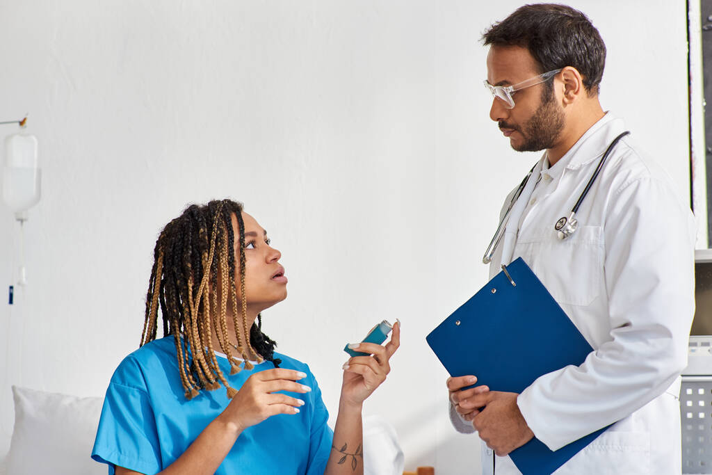 nuori intialainen lääkäri opettaa hänen sairas afrikkalainen amerikkalainen naispotilas miten käyttää astma-inhalaattoria - Valokuva, kuva